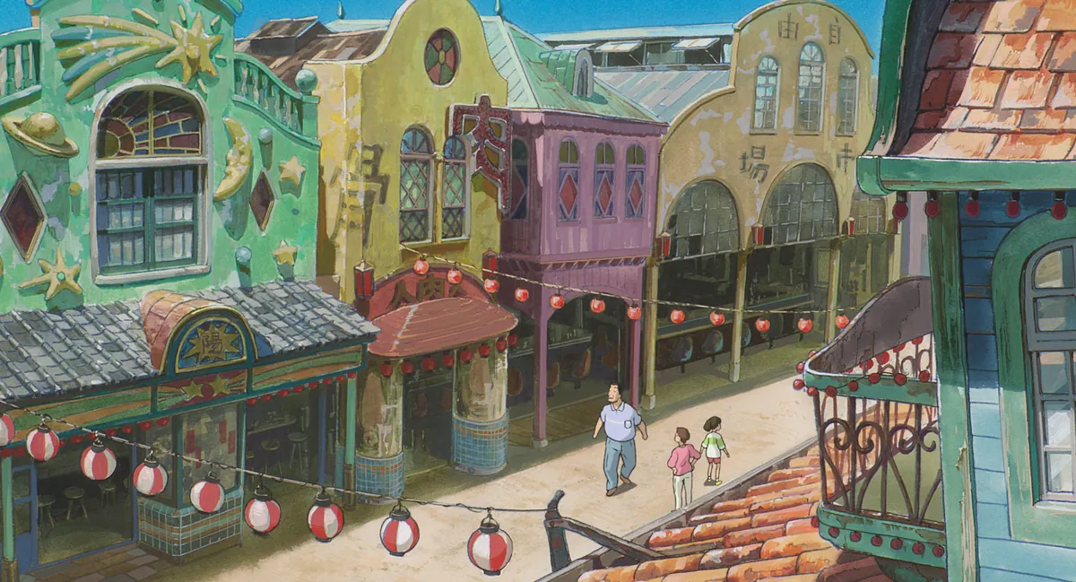 Cena oficial de A Viagem de Chihiro: Chihiro e os pais andam por uma rua de prédios coloridos enfeitada com lanternas vermelhas