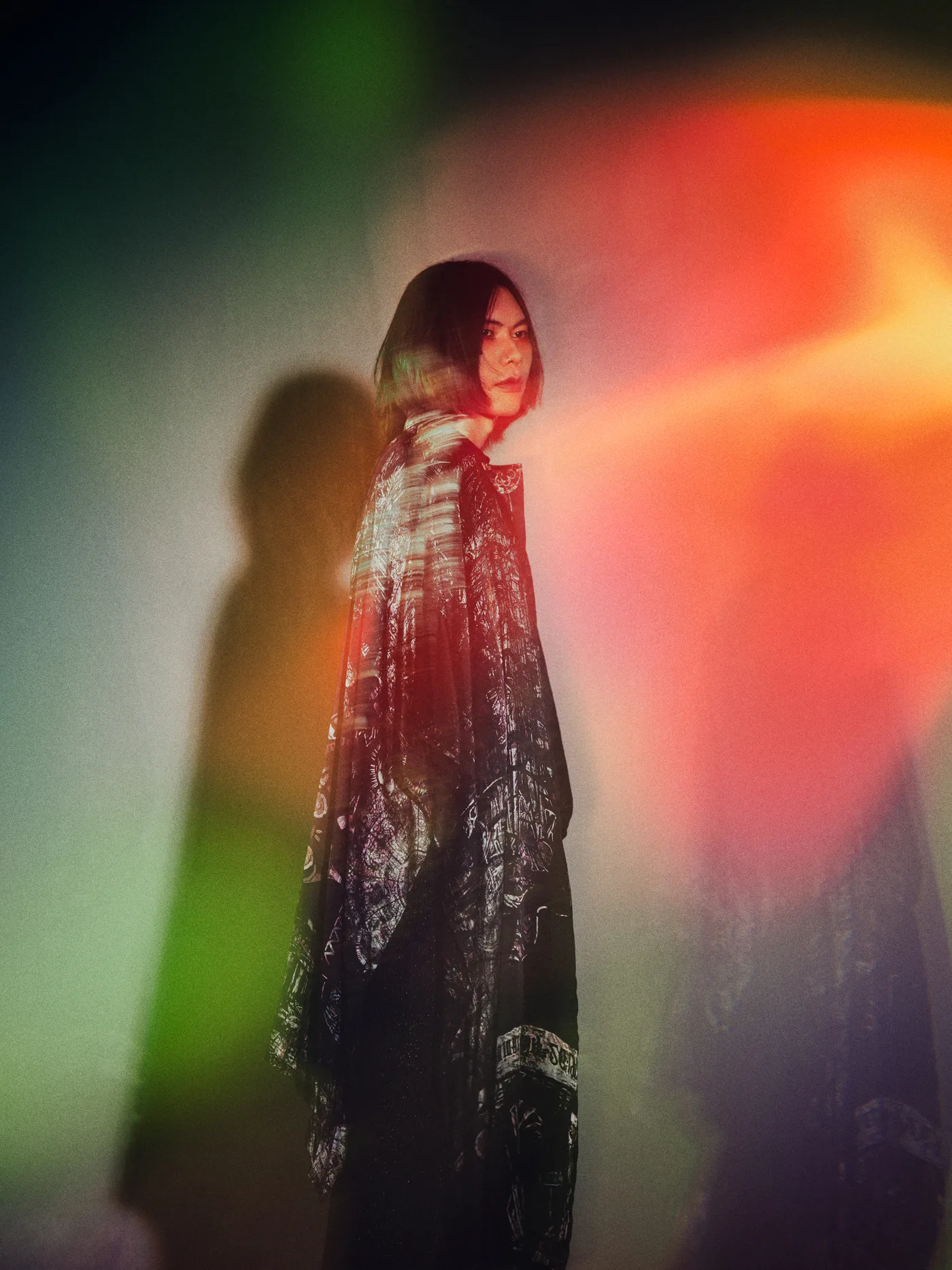 Kenshi Yonezu em foto oficial de divulgação, de pé, com luzes coloridas atrás